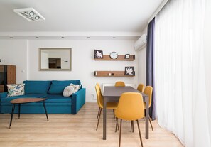 A modern living room with a blue sofa, a wooden coffee table, and a dining area with a table and yellow chairs. - Siekierki Serene Apartment (Warszawa)