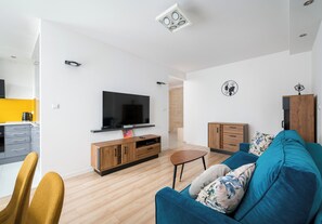 A modern living room with a flat-screen TV, wooden furniture, and a blue sofa. - Siekierki Serene Apartment (Warszawa)