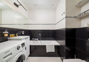 A modern bathroom with a washing machine, a bathtub, and a toilet. - Siekierki Serene Apartment (Warszawa)