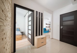 A modern interior with a wooden floor, a dark door, and a room with a bed and a blue sofa. - Siekierki Serene Apartment (Warszawa)