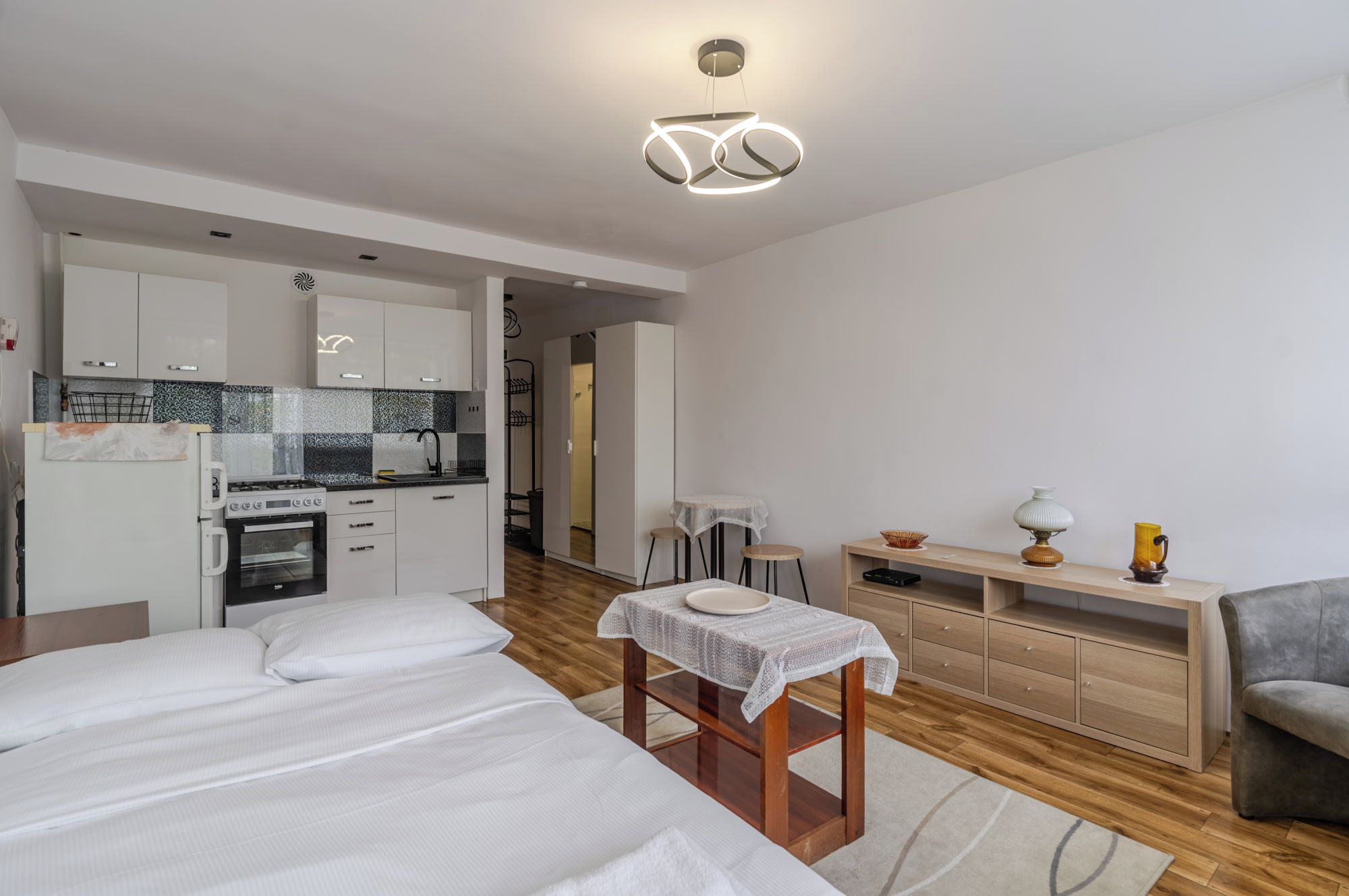 Une pièce moderne et bien éclairée, dotée d’une kitchenette, d’un coin repas avec une table et des chaises, et d’un lit avec une literie blanche.