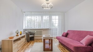 A modern living room with a wooden floor, a pink sofa, a grey armchair, a small wooden table, and a radiator. - Piastów Standard Studio (Katowice)