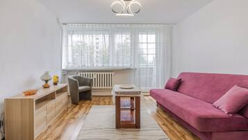 Un salon moderne avec un plancher en bois, un canapé rose, un fauteuil gris, une petite table en bois et un radiateur.