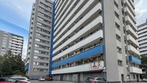 A multi-story residential building with balconies, a parking area, and a sign indicating the building's name. - Piastów Standard Studio (Katowice)
