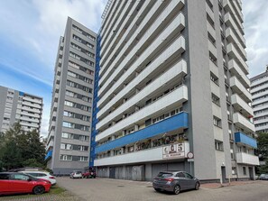 Un edifici d'habitatges de diversos pisos amb balcons, una zona d'aparcament i un rètol amb el nom de l'edifici.