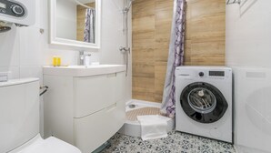 A compact bathroom with a toilet, sink, shower, and a washing machine. - Piastów Standard Studio (Katowice)