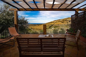 A covered outdoor seating area with a bench, chairs, and a table. - C/da Pozzetti Apartment (Lascari)