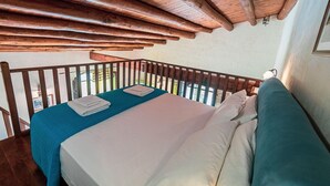 Habitació amb llit, balcó i bigues de fusta.
