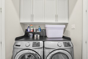 A laundry area with two front-loading washing machines, a drying rack, and a cabinet above. - Luxury Retreat Near Memorial & Heights. Sleeps 8 with Wellness Studio (Houston)