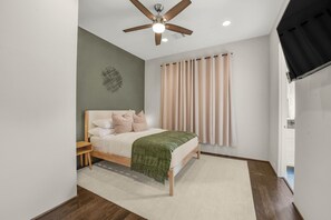 Ein Schlafzimmer mit einem Bett, einem Deckenventilator, einem Fenster mit Vorhängen und einer Tür.