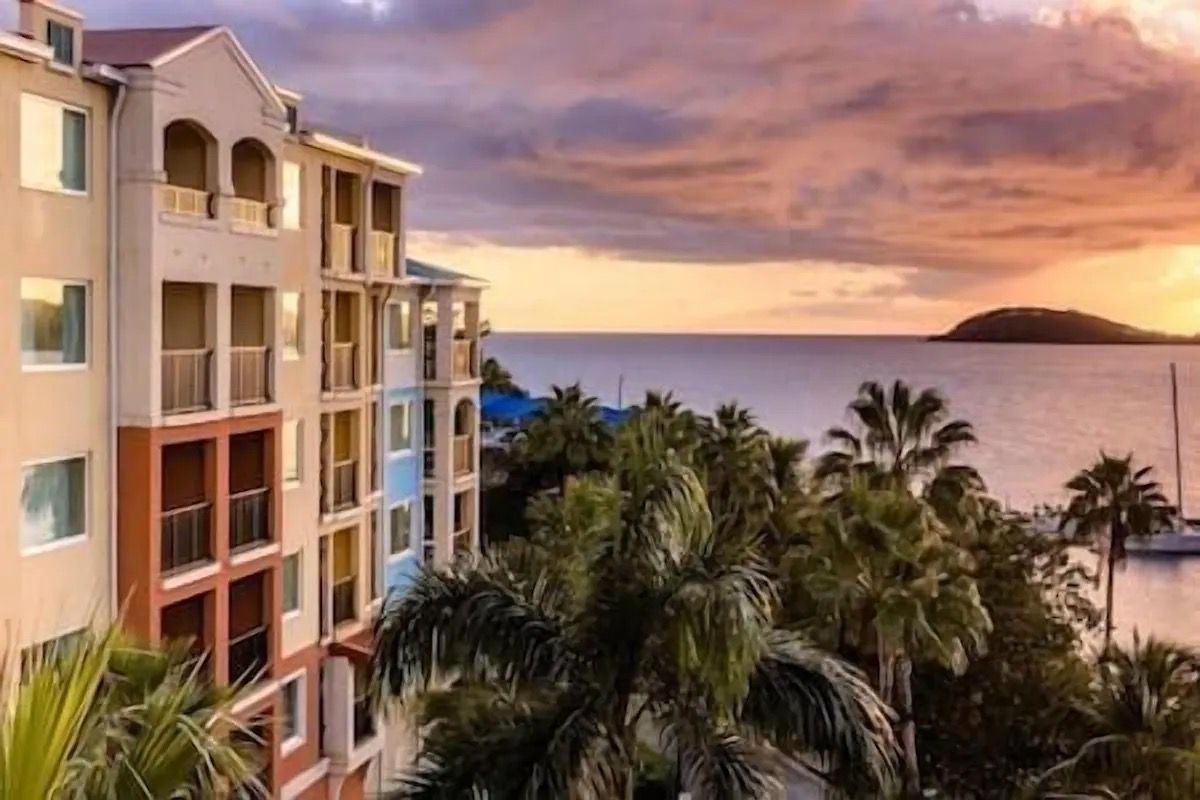 A multi-story hotel with balconies overlooking a body of water and palm trees.