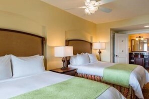 Une chambre d’hôtel avec deux lits, une table de chevet avec une lampe, un ventilateur de plafond et une vue sur la salle de bain.