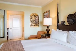 A hotel room with a bed, a nightstand, a lamp, a chair, a door, and a decorative wall piece.