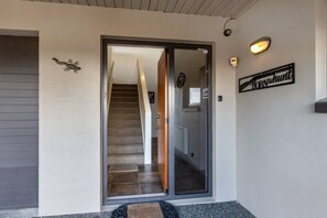 Una entrada moderna con puerta de vidrio, escalera de madera y un letrero de bienvenida.