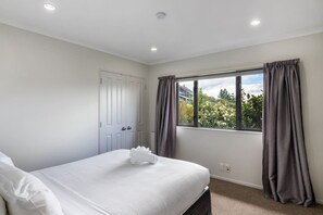 Un dormitorio con cama, ventana con cortinas, una puerta y vistas al exterior con vegetación.