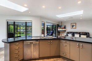 Una cocina moderna con lavavajillas integrado, encimera negra y vistas al jardín trasero a través de amplios ventanales.