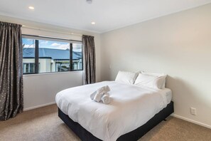 A hotel room with a large bed, a window with curtains, and a view of buildings outside.