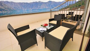 Un balcón con mobiliario de mimbre, una mesa de vidrio y vistas a montañas y un lago.
