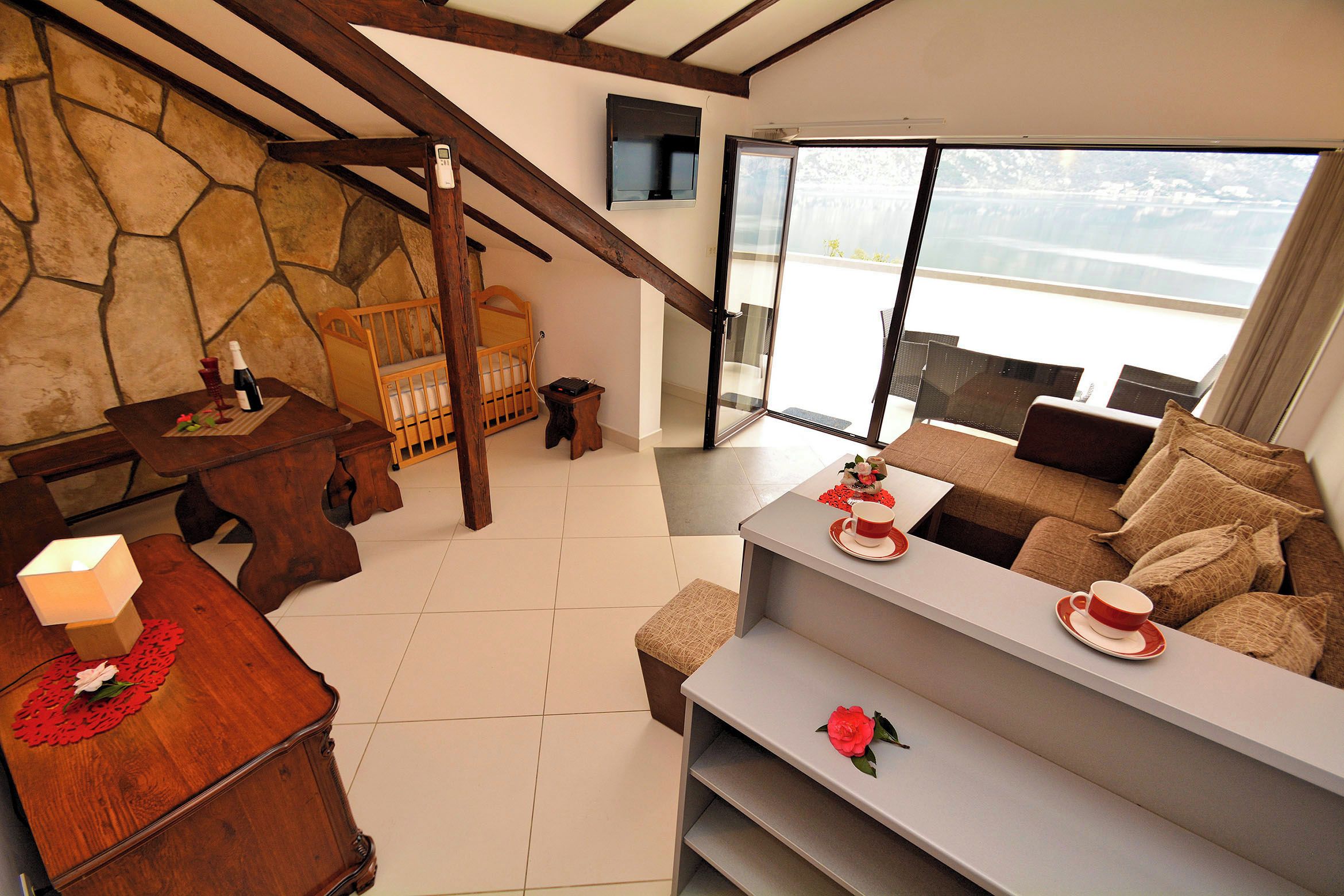 A modern living room with a stone wall, wooden furniture, a balcony with a view, and a cozy seating area.