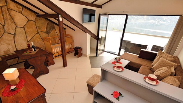 Una sala de estar moderna con pared de piedra, muebles de madera, un balcón con vistas y un rincón de descanso acogedor.