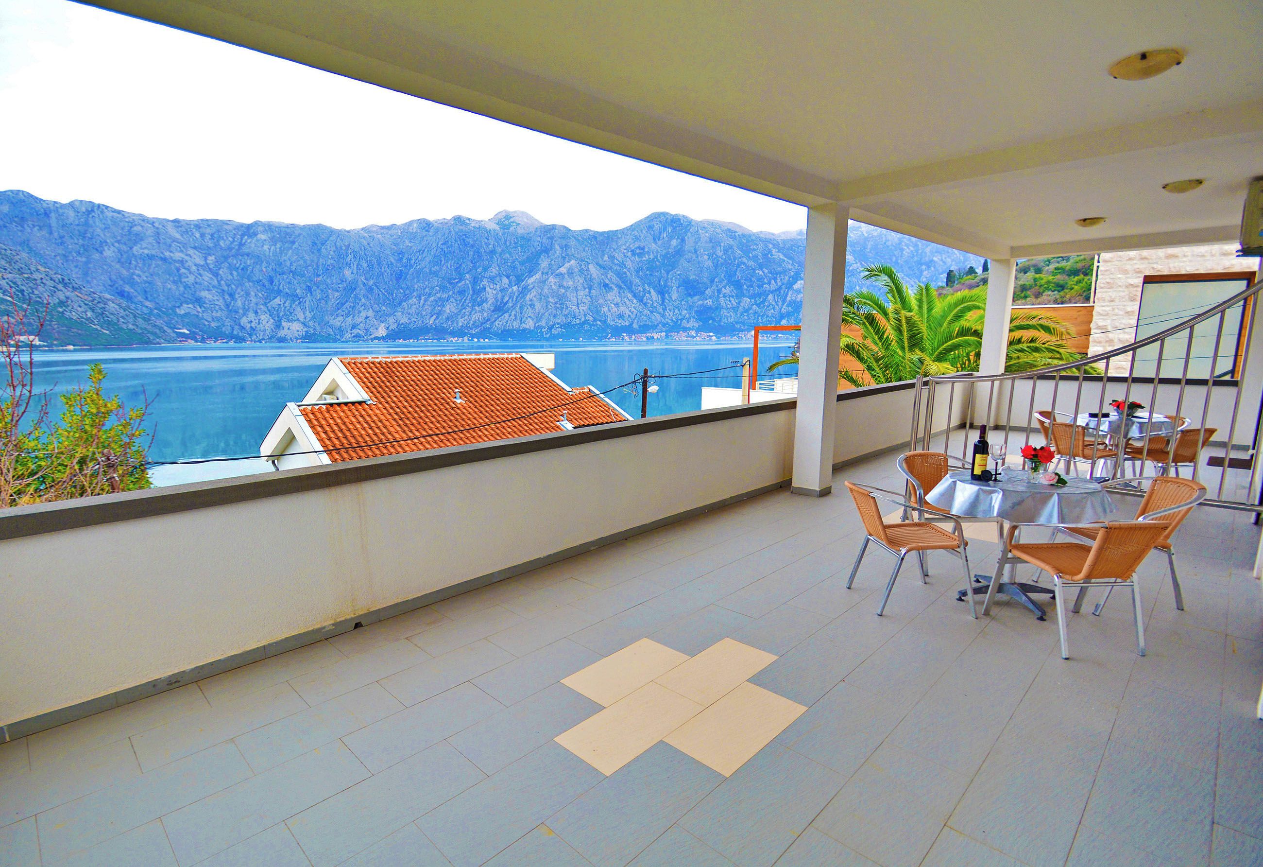 A balcony with a table and chairs, overlooking a body of water and mountains.