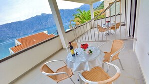 Un balcón con una mesa para dos, sillas de mimbre y vistas al mar y a las montañas.