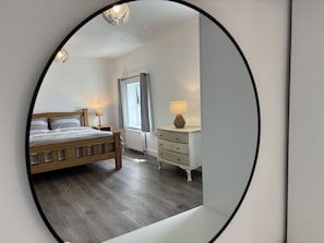 Een slaapkamer met een houten bed, bedlampjes, een dressoir en een raam met gordijnen.