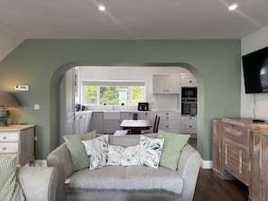 A cozy living room with a sofa, a coffee table, and a TV mounted on the wall. - Cottage 519 - Kilkieran - sleeps 6 guests  in 3 bedrooms (Kilkerrin)