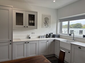 Een moderne keuken met witte kastjes, een eettafel en een raam met uitzicht op gebouwen.