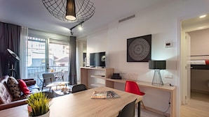 A modern living room with a sofa, dining table, and chairs, a TV, and a large window with a view of buildings. - Hot Jazz 51 (Barcelona)