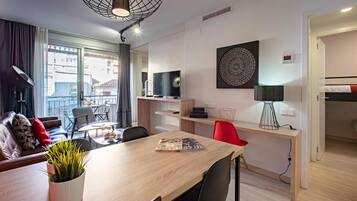Een moderne woonkamer met een bank, een eettafel, stoelen, een televisie en een groot raam met uitzicht op gebouwen.