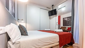 A hotel room with a bed, a small round table, a television mounted on the wall, and a door with a handle. - Hot Jazz 51 (Barcelona)