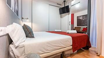 Een hotelkamer met een bed, een klein rond tafeltje, een aan de muur bevestigde televisie en een deur met een hendel.