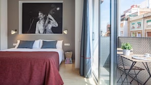 A bedroom with a bed, pillows, a nightstand, a window with curtains, and a view of buildings outside. - Hot Jazz 51 (Barcelona)