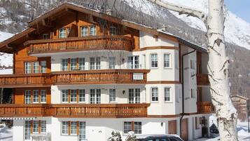 A multi-story hotel with wooden balconies and large windows, surrounded by snow-covered mountains.