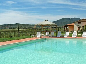 A swimming pool with lounge chairs and a gazebo, surrounded by a landscaped garden and a view of hills. - A5 - Three Bedroom (Grosseto)