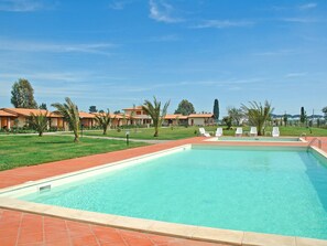A swimming pool with a tiled deck, surrounded by lounge chairs and a grassy area with trees. - A5 - Three Bedroom (Grosseto)