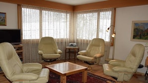 Un salon avec quatre fauteuils en cuir beige, une table basse en bois et un tapis rouge à motifs.