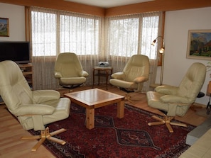 A living room with four beige leather chairs, a wooden coffee table, and a red patterned rug. - Aegertenstrasse 18 # 1 - Two Bedroom (Lenk)