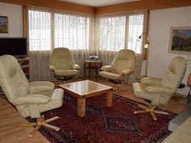 Un salón con cuatro sillones de cuero color beige, una mesa de centro de madera y un tapete con estampado rojo.
