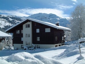 A two-story chalet with a sloped roof, surrounded by snow-covered mountains and trees. - Aegertenstrasse 18 # 1 - Two Bedroom (Lenk)