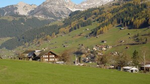 Un paysage rural avec un village, des champs verdoyants et des montagnes en arrière-plan.