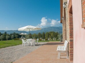 An outdoor seating area with tables and chairs, a white umbrella, and a view of mountains in the background. - Collina - One Bedroom (Perugia)