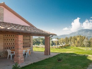 A covered patio area with brick walls and a tiled roof, overlooking a grassy landscape with trees and mountains. - Collina - One Bedroom (Perugia)