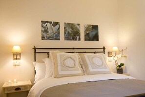 A bedroom with a bed, two bedside tables, wall-mounted lamps, and three framed pictures on the wall. - Venturina - One Bedroom (Campiglia Marittima)