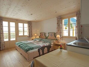 A bedroom with a bed, bedside table, lamp, and a view of the outdoors through a window. - Mutthorn - One Bedroom (Lauenen)