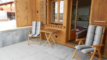 Ein Holzhaus mit zwei Stühlen und einem Tisch, einer Tür zu einem Schlafzimmer und Blick auf ein Gebäude.
