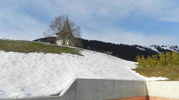 Schneebedeckte Landschaft mit einem Gebäude auf einem Hügel, blauem Himmel und einer Betonkonstruktion im Vordergrund.