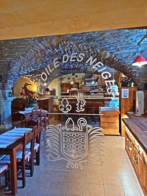Zona de bar con un muro de piedra de fondo, mobiliario de madera y un tablero de menú visible.