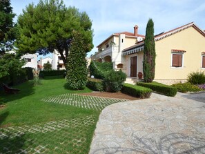 A residential property with a paved driveway, well-maintained lawn, and a variety of shrubs and trees. - Stana - One Bedroom (Zadar)